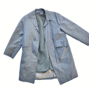 May include: A light blue, double-breasted coat with a soft, fuzzy interior lining. The coat has two front pockets and a classic lapel collar. The coat is laid flat on a white surface.