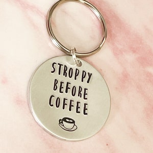 May include: Silver keychain with a round tag that says "STROPPY BEFORE COFFEE" with a small coffee cup icon.