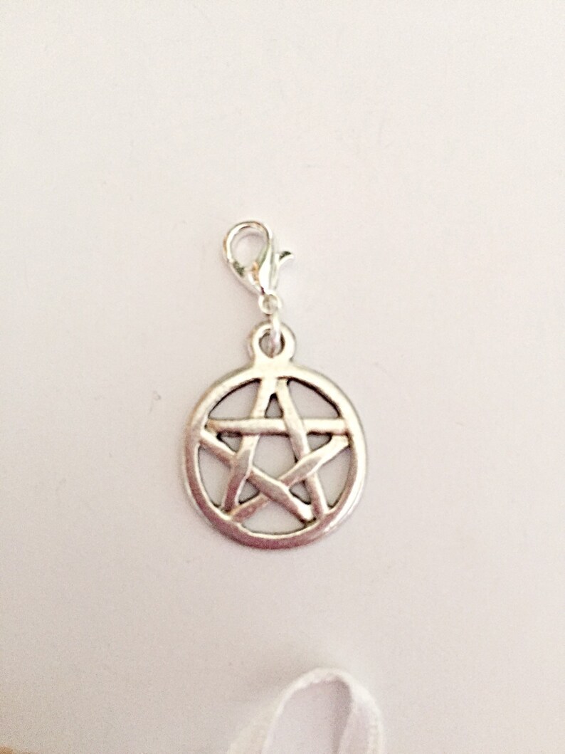 May include: A silver-colored charm with a pentagram design. The charm is circular with a five-pointed star inside a circle. It has a lobster clasp for easy attachment to a bracelet or necklace.