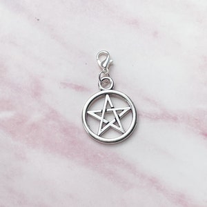 May include: A silver-colored pentagram charm with a lobster clasp. The five-pointed star is set within a circular frame. The charm is shown against a pink and white marble background.
