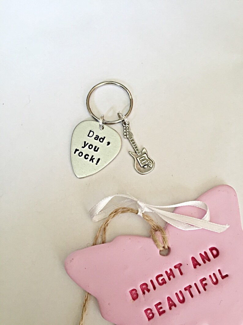 May include: A silver guitar pick keychain with the text "Dad, you rock!" and a small silver guitar charm. A pink ceramic butterfly ornament with the text "Bright and Beautiful" is also shown.
