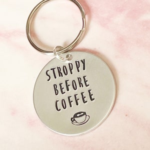 May include: Silver keychain with a round tag that says "STROPPY BEFORE COFFEE" with a small coffee cup icon.