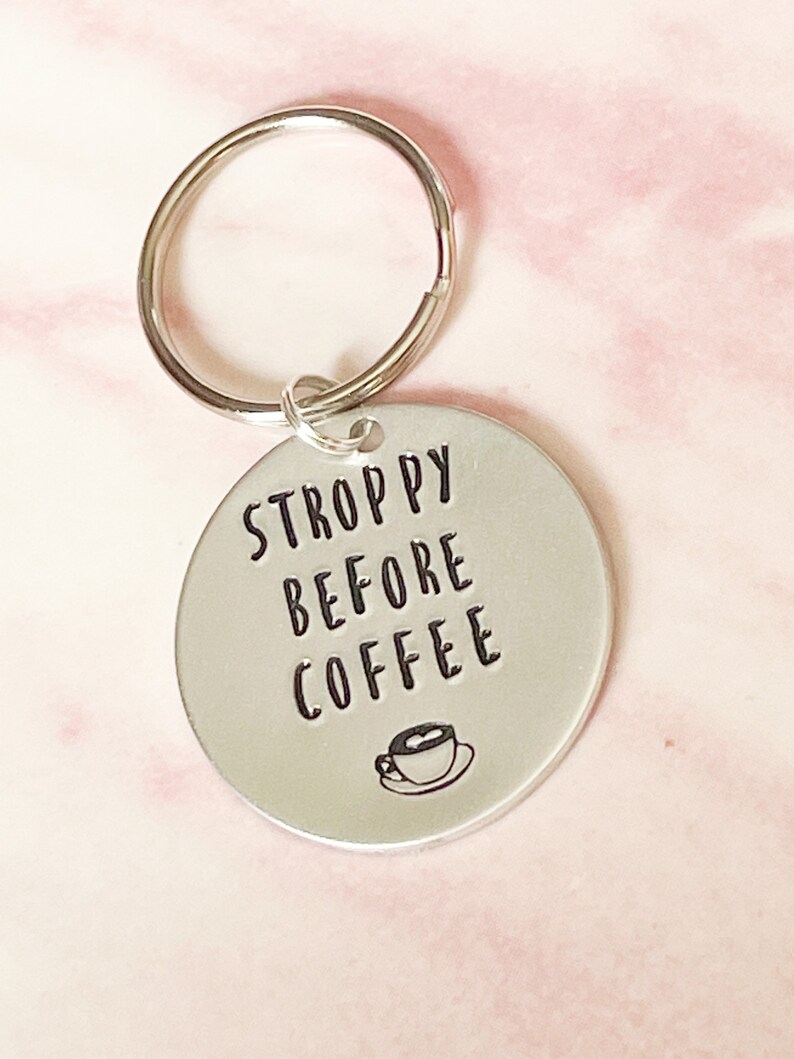 May include: Silver keychain with a round tag that says "STROPPY BEFORE COFFEE" with a small coffee cup icon.
