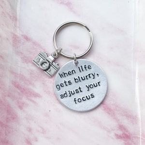 May include: Silver keyring with a camera charm and a round tag that says "When life gets blurry, adjust your focus".