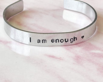 May include: Silver metal bracelet with the inscription "I am enough" and a small heart symbol.