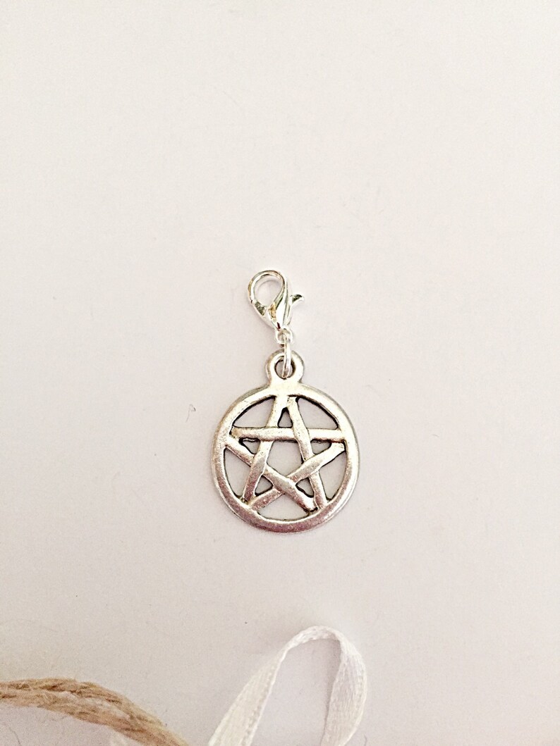 May include: Silver-toned charm featuring a pentagram design within a circular frame. The charm is attached to a clasp, suitable for use on a bracelet or necklace. The charm is made of metal and has a vintage appearance.