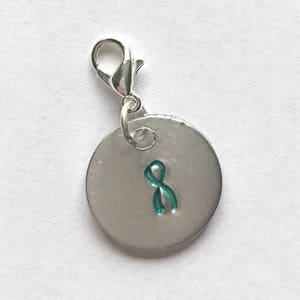 May include: Silver charm with a teal ribbon on a round disc. The charm has a silver lobster clasp.