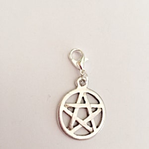 May include: Silver-colored charm featuring a pentagram design within a circular frame. The charm is attached to a lobster clasp for easy attachment to a necklace or bracelet. The charm is made of metal and has a shiny finish.