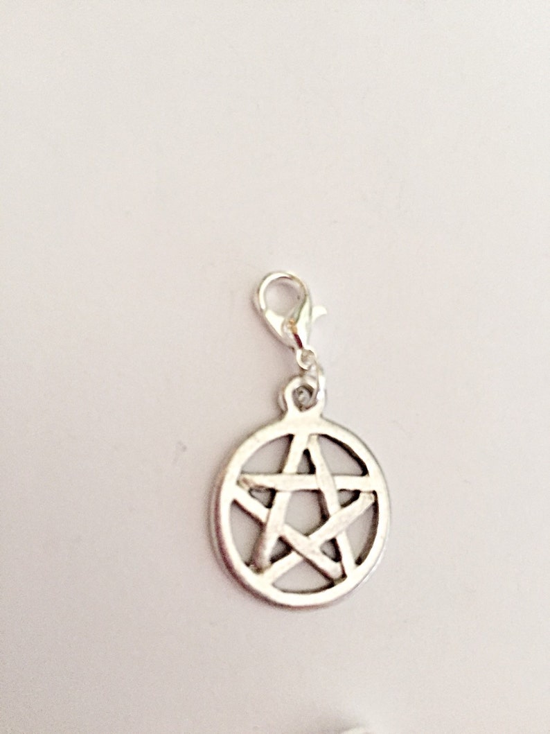 May include: Silver-colored charm featuring a pentagram design within a circular frame. The charm is attached to a lobster clasp for easy attachment to a necklace or bracelet. The charm is made of metal and has a shiny finish.