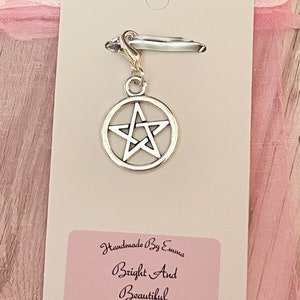 May include: A silver-colored charm with a pentagram design, attached to a clasp. The charm is on a white card with a pink label that reads "Handmade By Emma Bright And Beautiful". The background is a soft pink.