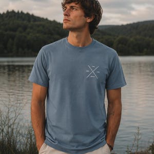 May include: A dusty blue short-sleeve t-shirt featuring a small white graphic on the left chest. The graphic consists of two crossed lines forming an X with the words THE, WAY, TRUTH, and LIFE positioned between the lines of the cross.