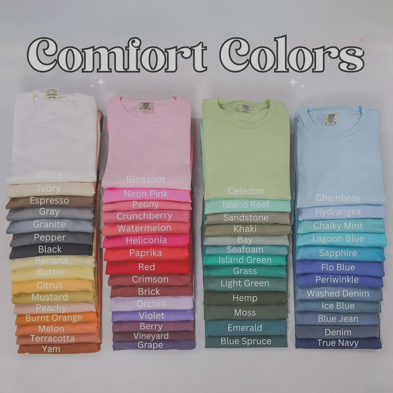 May include: A display of Comfort Colors t-shirts in a variety of shades, such as white, pink, green, and blue. Each stack shows a folded t-shirt with a colour name label underneath. The image presents a wide spectrum of colours.