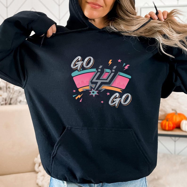 Puede incluir: Sudadera con capucha negra con un gr&aacute;fico colorido que dice "GO GO" y un emblema estilizado. El dise&ntilde;o incluye detalles en rosa, turquesa y naranja con rayos y estrellas. La sudadera tiene un bolsillo delantero y una capucha con cord&oacute;n.