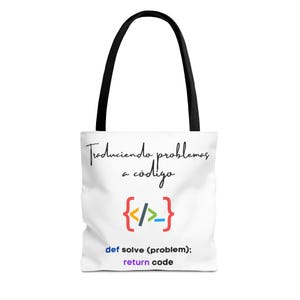 Op de afbeelding: Witte draagtas met zwarte handvatten. De tas heeft de tekst "Traduciendo problemas a código" en een kleurrijk codesymbool. Daaronder staat de tekst "def solve (problem): return code."