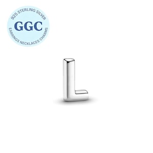 Può includere: Un ciondolo a forma di lettera "L" in argento lucido. Il ciondolo è realizzato in metallo lucido e ha un design squadrato e arrotondato. Un logo circolare con la scritta "925 Sterling Silver" e "GGC" si trova nell'angolo in alto a sinistra. Il ciondolo è per orecchini, collane e ciondoli.