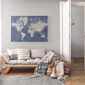 May include: A framed world map in shades of blue and beige hangs above a wooden sofa with pillows and a blanket. The room features a rug, a small side table, and open white doors, creating a cozy and inviting living space. The floor is made of wood.
