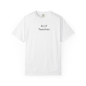 Puede incluir: Camiseta blanca con el texto negro "R.I.P Twenties". La camiseta tiene cuello redondo y mangas cortas. El texto está centrado en la parte delantera de la prenda.