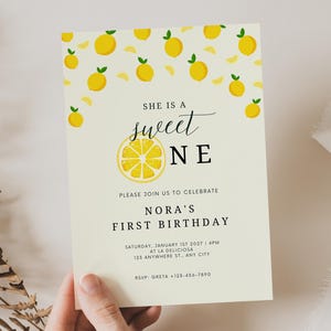 Könnte beinhalten: Eine cremefarbene Geburtstagseinladung mit Zitronenmotiv. Der Text "SHE IS A sweet ONE" wird über den Worten "PLEASE JOIN US TO CELEBRATE NORA'S FIRST BIRTHDAY" angezeigt. Die Einladung enthält Datum, Uhrzeit und Ort.