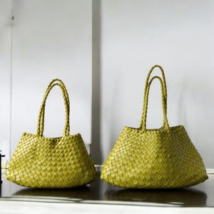 Pode incluir: Duas sacolas tote tecidas em um tom verde oliva claro. As sacolas têm alças trançadas e um design de tecido de cesta. As sacolas são de tamanhos diferentes, a sacola maior à direita e a menor à esquerda.