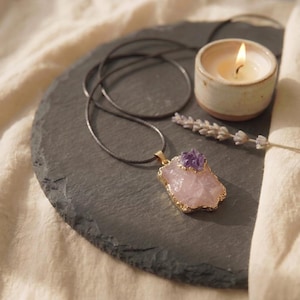 Rosenquarz Amethyst Talisman Kette flach liegend auf Schieferplatte neben brennender Kerze und Lavendelblüte