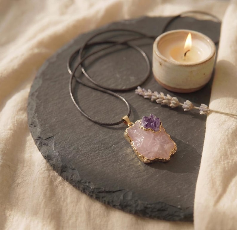 Rosenquarz Amethyst Talisman Kette flach liegend auf Schieferplatte neben brennender Kerze und Lavendelblüte