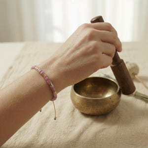 Frauenhand mit rosa Rhodonit Armband beim Anschlagen einer tibetischen Meditations Klangschale.
