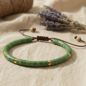 Nahaufnahme eines Serpentin Armbands mit flachen 6mm Perlen in moosgrünen Natursteintönen auf beigem Leinenstoff.