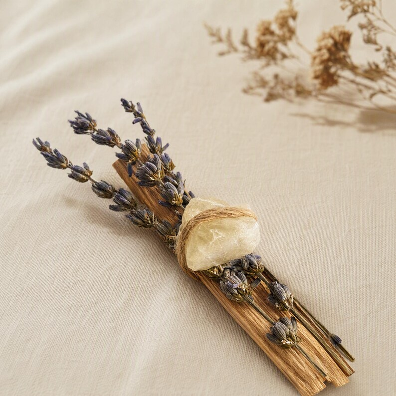 Draufsicht auf ein Palo Santo Räucherbündel mit lila Lavendelblüten und einem hellen Citrin Rohstein, sanft gebunden mit Naturkordel auf beigem Leinenstoff.