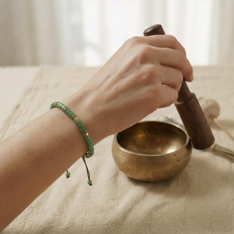 Eine Klangschale wird geschlagen. Der Arm ist mit dem Serpentine Armband im Boho Stil geschmückt.