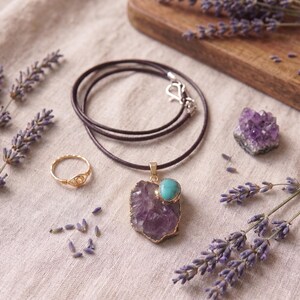 Flatlay-Ansicht der Amethyst-Talisman-Halskette mit Lederband, drapiert mit Goldring, Amethyst-Kristall und Lavendelblüten.