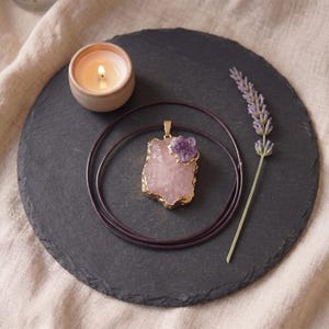 Talisman Kette mit Rosenquarz Amethyst flach liegend auf Schieferplatte neben brennender Kerze und Lavendelblüte