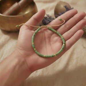 Grünes Edelstein Armband aus Serpentin flach liegend neben einer matten Holzschale und getrockneten Gräsern.