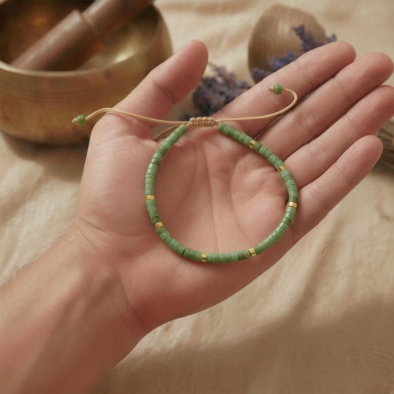 Grünes Edelstein Armband aus Serpentin flach liegend neben einer matten Holzschale und getrockneten Gräsern.