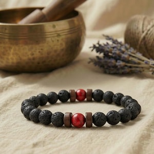 Schwarzes Lavastein Armband mit zwei roten Jaspis Perlen auf grobem Leinenstoff.