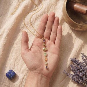 Filigrane vergoldete Chakra Y-Kette mit funkelnden Pavé-Fassungen auf dunklem Schieferuntersetzer im sanften Kerzenschein.