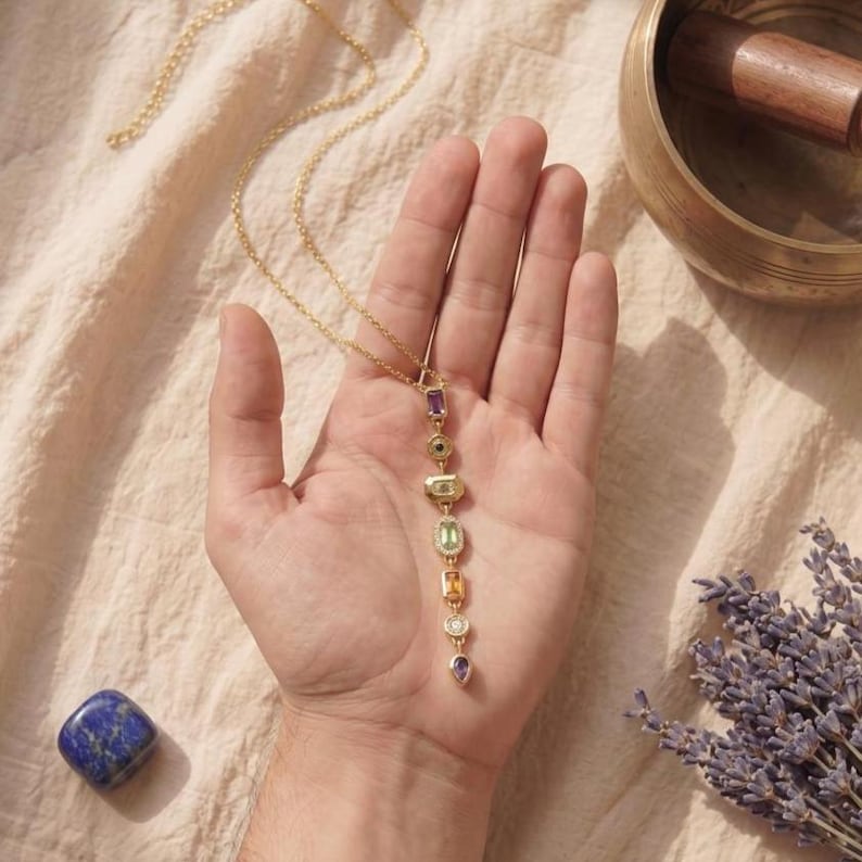 Filigrane vergoldete Chakra Y-Kette mit funkelnden Pavé-Fassungen auf dunklem Schieferuntersetzer im sanften Kerzenschein.