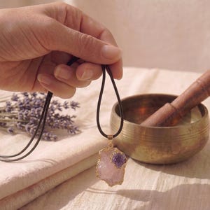 Rosenquarz Amethyst Anhänger Kette in Goldfassung gehalten in der Hand neben tibetischer Klangschale und getrocknetem Lavendel