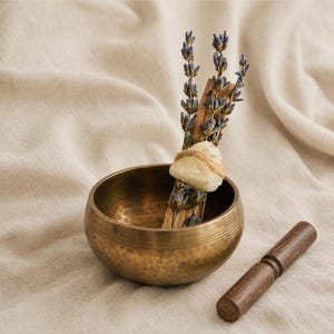 Handgebundenes Palo Santo Räucherbündel mit getrocknetem Lavendel und gelbem Citrin Rohkristall, aufrecht arrangiert in einer traditionellen Klangschale aus Messing mit Holzklöppel.