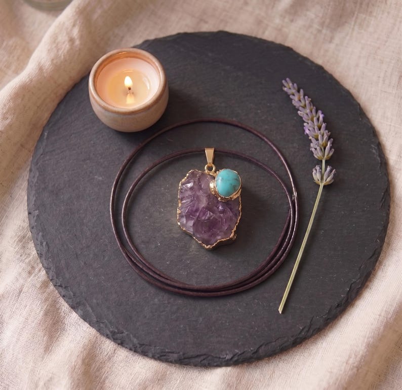 Zentrierte Draufsicht auf den Amethyst-Türkis-Talisman auf dunklem Schieferuntersetzer mit Kerzenschein und Lavendelzweig.