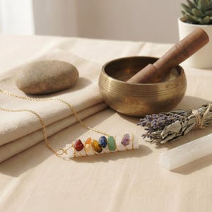 Selenit-Chakra-Anhänger an goldener Kette flach arrangiert neben Klangschale und Räucherwerk.