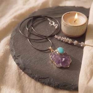 Rohstein Amethyst Kette mit gefasstem Türkis auf einer runden Schieferplatte neben einer brennenden Kerze und getrocknetem Lavendel.
