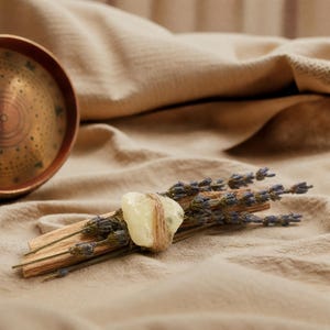 Natur-Räucherbündel aus duftendem Palo Santo Holz, Lavendel und einem Citrin Edelstein, drapiert neben einer runden Schamanentrommel auf hellem Stoff.