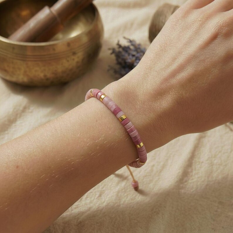 Rhodonit Armband aus feinen rosa Scheibenperlen getragen am Frauenarm in warmer Studioatmosphäre.