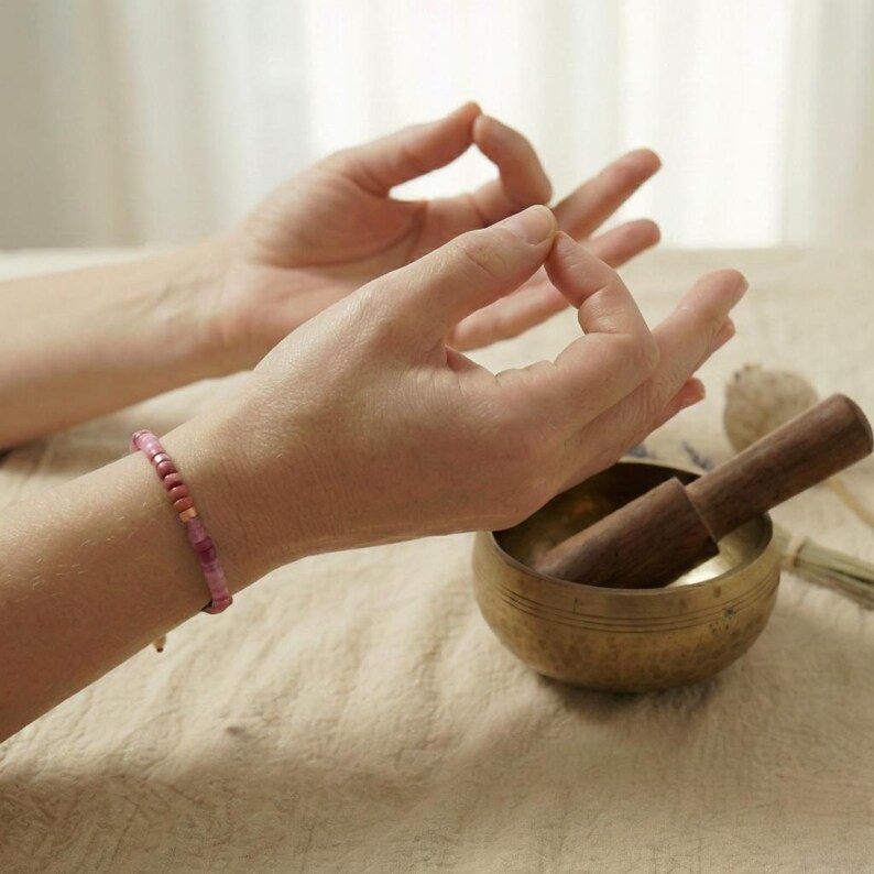 Zartes rosa Edelsteinarmband am Handgelenk während einer Yoga Meditation in Mudra Handhaltung.