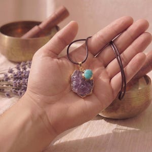 Amethyst Talisman Anhänger mit Türkis-Akzent liegt in einer Handfläche zum Größenvergleich, arrangiert mit Klangschale und Lavendel.