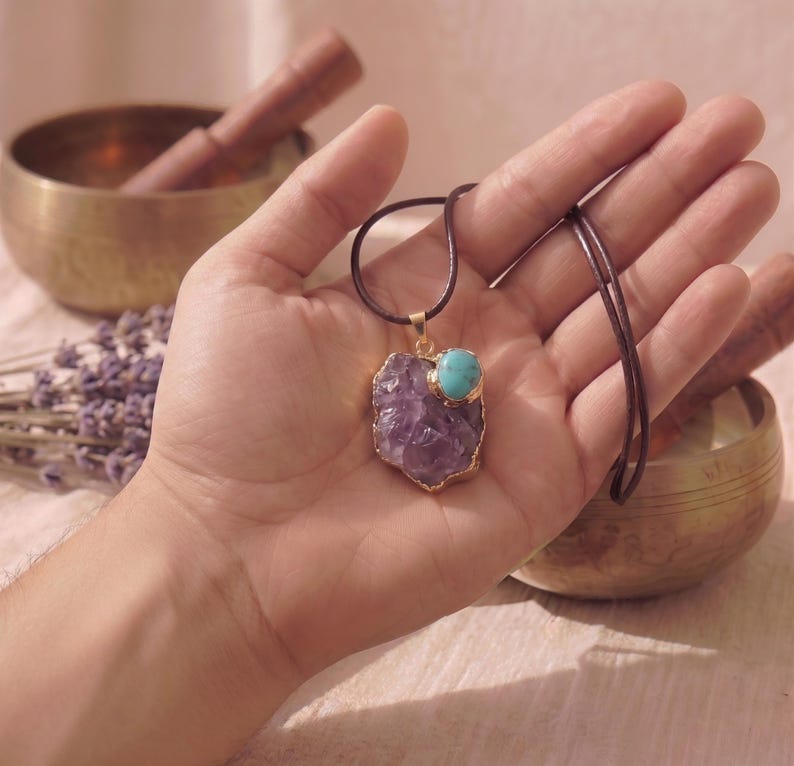 Amethyst Talisman Anhänger mit Türkis-Akzent liegt in einer Handfläche zum Größenvergleich, arrangiert mit Klangschale und Lavendel.
