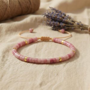 Nahaufnahme des flachen Rhodonit Naturstein Armbands mit Schiebeknoten auf hellem Leinenstoff.