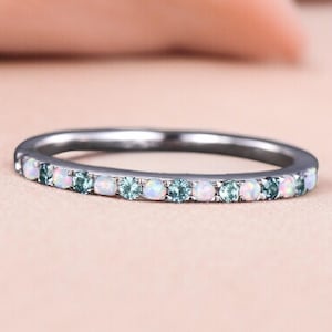 May include: A silver ring with a band of alternating white and blue gemstones. The gemstones are round and set closely together, creating a continuous line of color around the ring.
