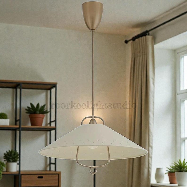 May include: Cream-coloured pendant light with a conical shade and a metal frame. The light fixture hangs from a thin cord and has a metallic finish. The design is simple and modern, suitable for various interior styles.