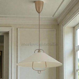 May include: Cream-coloured pendant light with a wide, conical shade and a metal frame. The light fixture is suspended from the ceiling by a thin rod and a decorative canopy. The text "roorkeelightstudio" is visible on the shade.